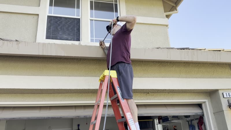 Wesley Cable cleaning second-story gutters from a ladder