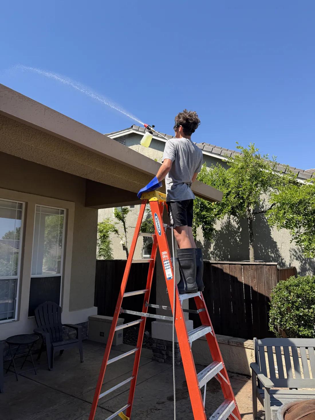 Cable crew member on a ladder applying wash solution above the eave of a stucco home